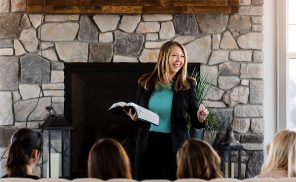 Jenny at a training teaching in front of stone fireplace with attendees in the foreground sitting on a couch
